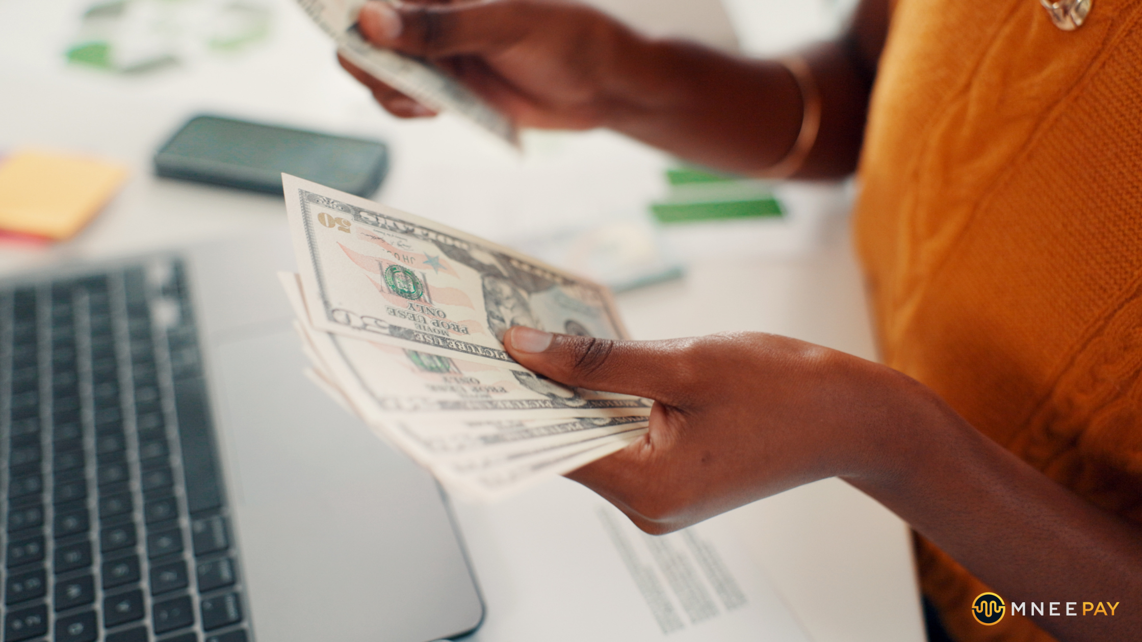 Merchant counting money while reviewing delayed payment settlement on laptop